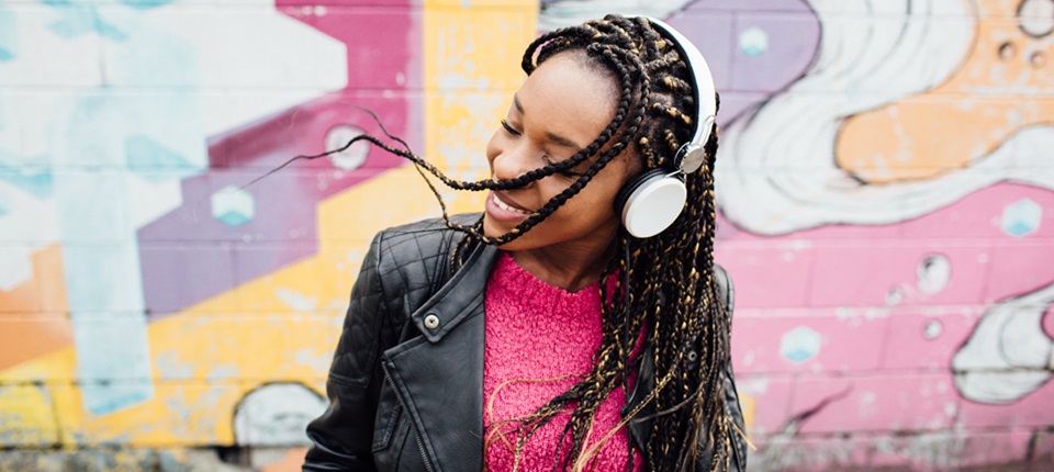 African woman wearing headphone having fun listening to music. Against brick wall colorful with graffiti art.