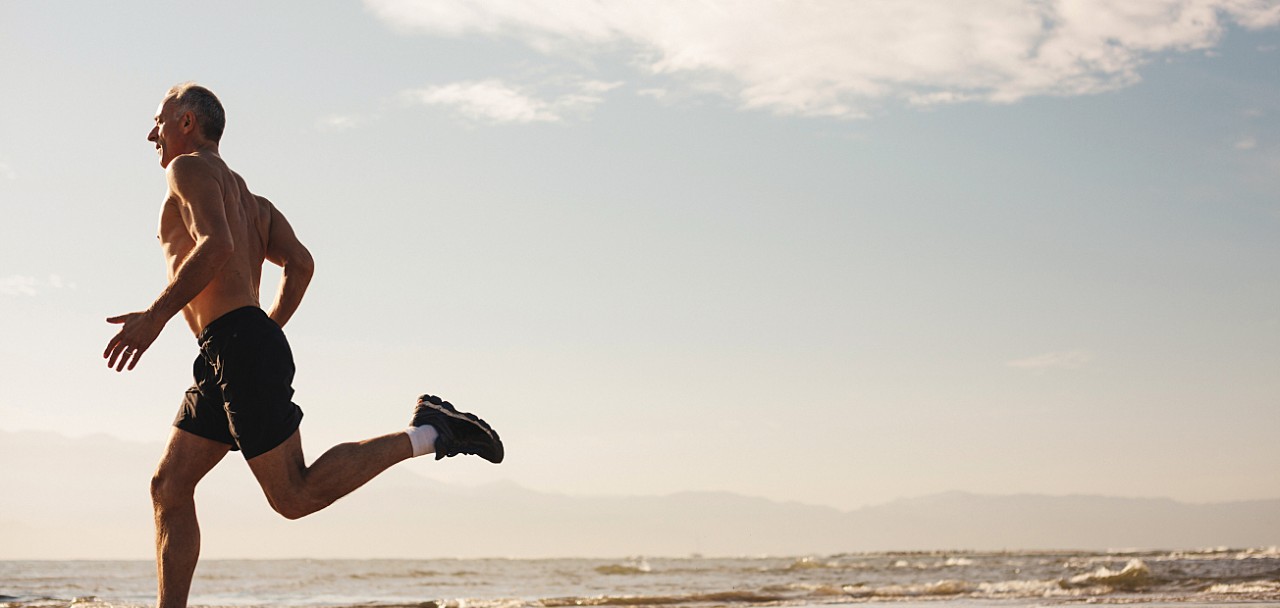 Active senior man - in great shape - running shirtless on beach in morning sunshine