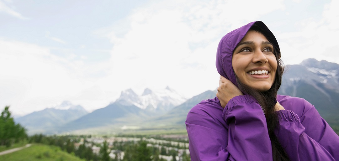 E5NGK7 Smiling woman in hooded jacket near mountains
