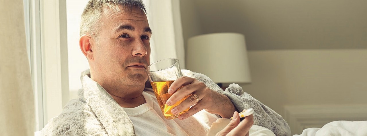 man sick in bed taking temperature drinking pedialyte
